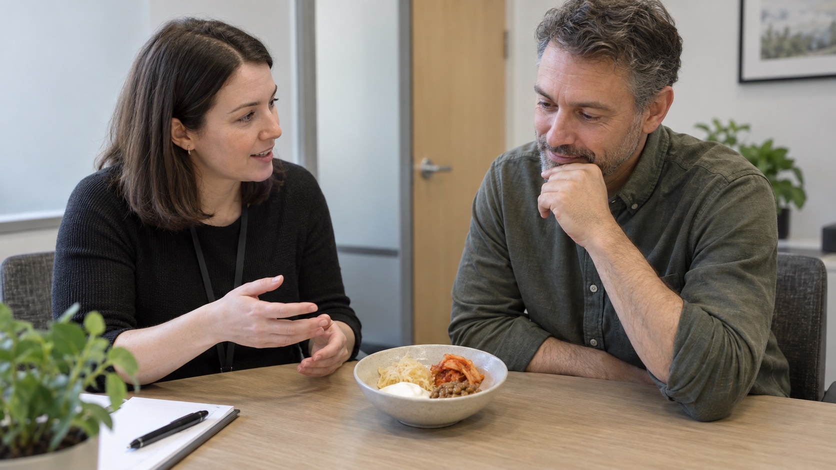 A researcher and adult discuss a small serving of fermented foods at a table.